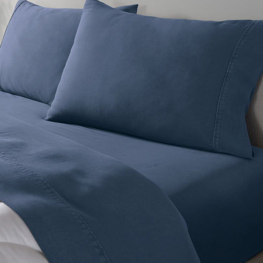 A close-up of a blue bedding set on a bed, showing a fitted sheet and two matching pillowcases.