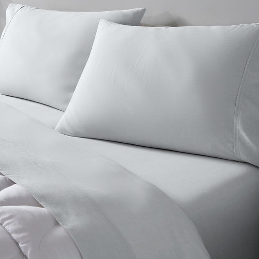 Light grey bedding set including two pillowcases and a matching sheet on a bed, photographed in a clean studio setting.
