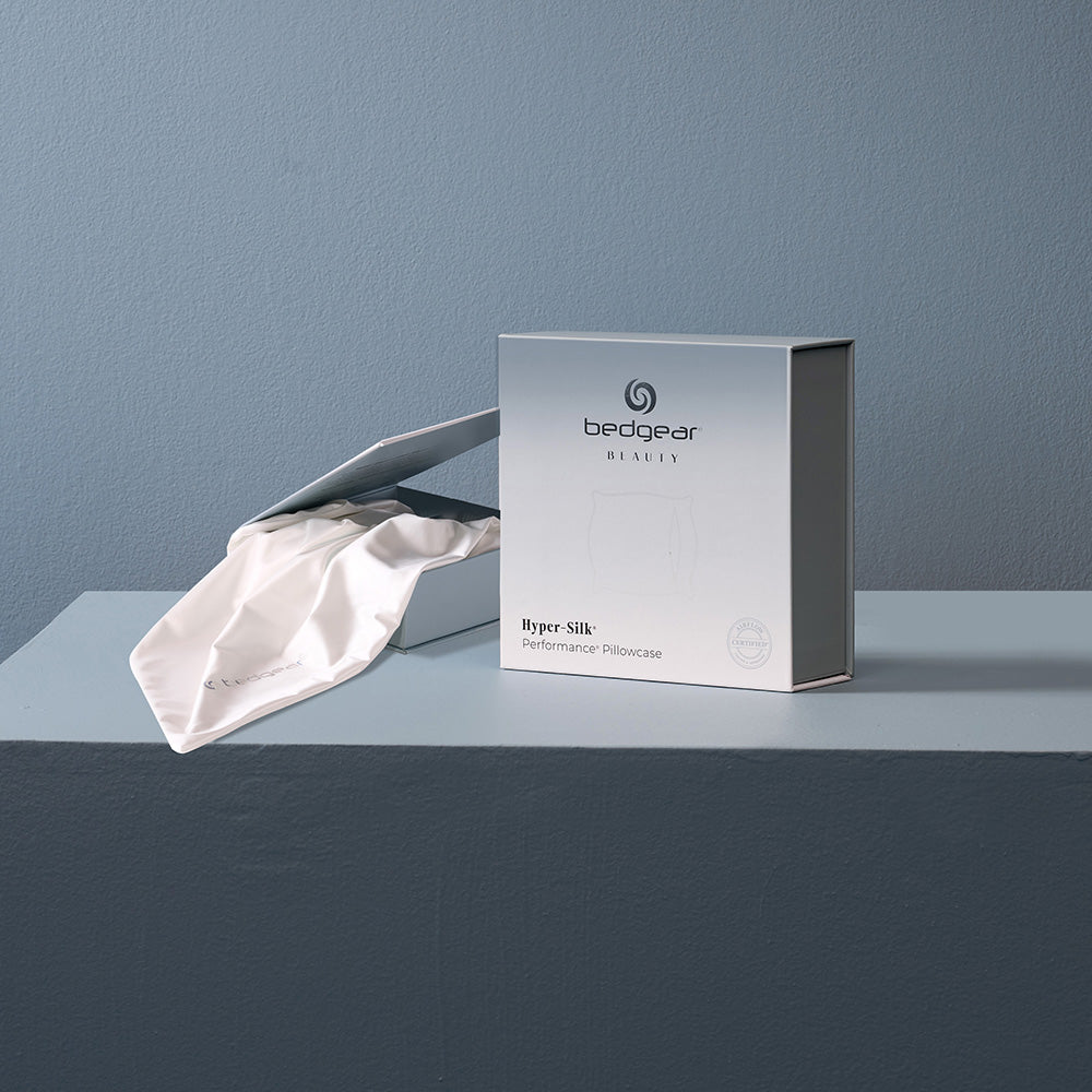 A white hyper silk pillowcase next to BEDGEAR's packaging. 