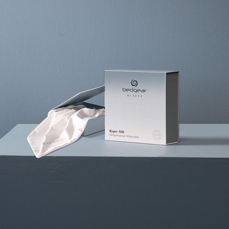 A white hyper silk pillowcase next to BEDGEAR's packaging. 