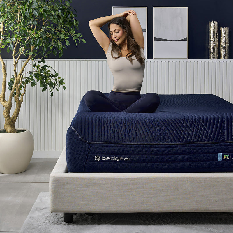 A woman sitting on an M3 Night Ice mattress. 