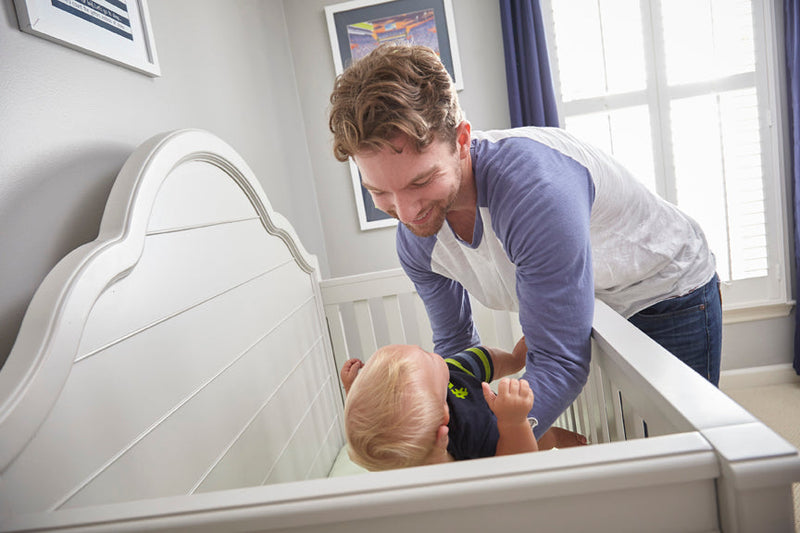 A man lowering his child into a crib. 