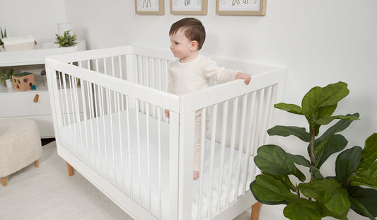 A baby standing in a crib with the appropriate crib mattress size. 