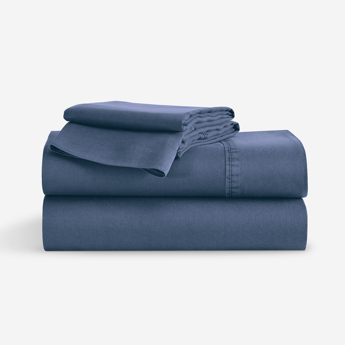 A stack of folded Indigo blue bedding, including  folded sheets and a folded pillowcase, shown on a clean white background.