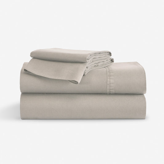 A stack of a folded bedding sheet set, in a light taupe-beige color, photographed against a seamless white studio background. "Stone"