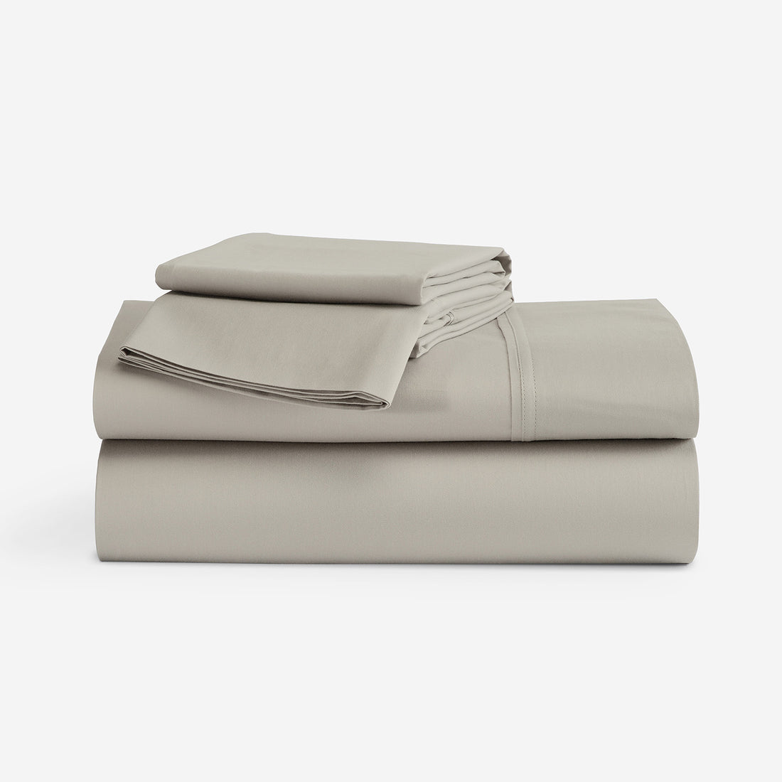 A stack of folded bedding sheets in a solid light taupe color, photographed on a seamless white studio background. "Taupe"