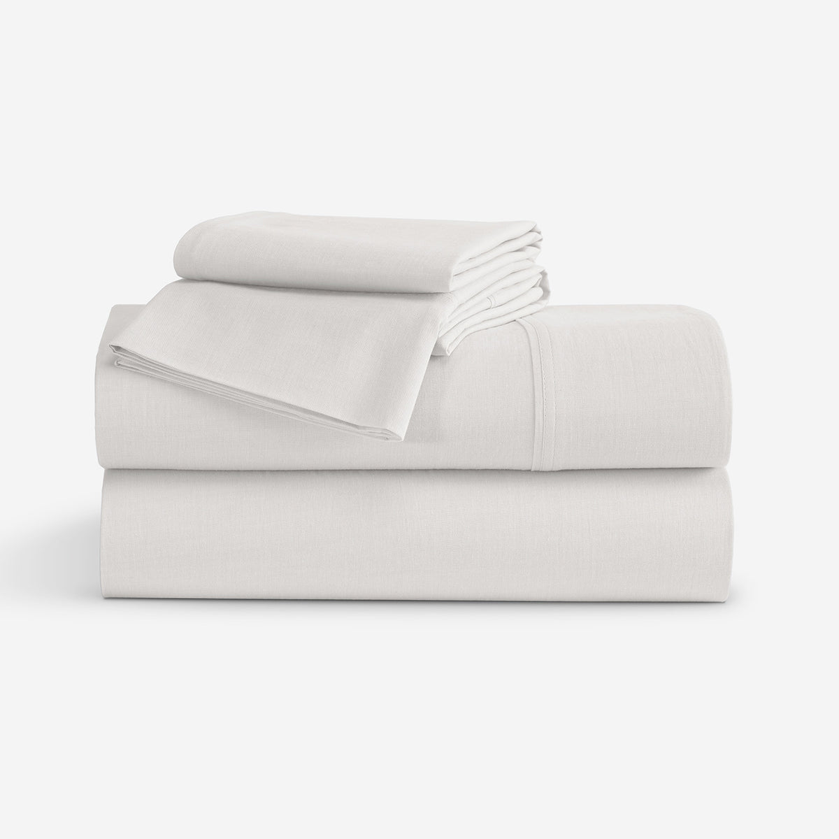 A stack of folded white bedding, including sheets and pillow cases, photographed on a clean white studio background.