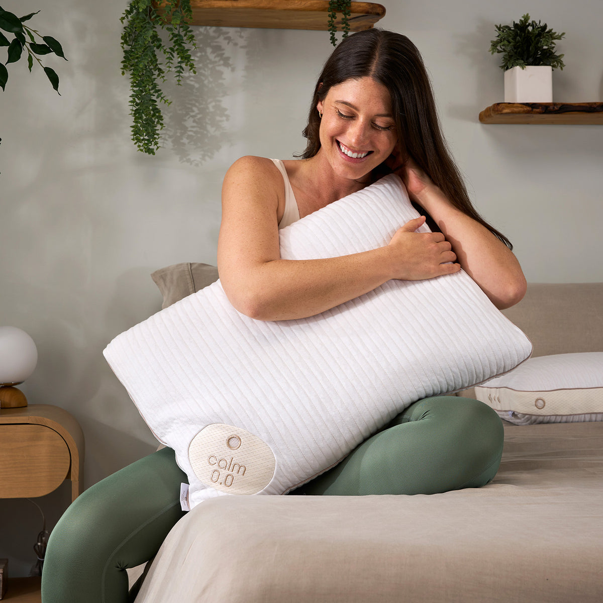 A woman hugging a Calm 0.0 Performance Pillow in a cozy, modern bedroom setting.