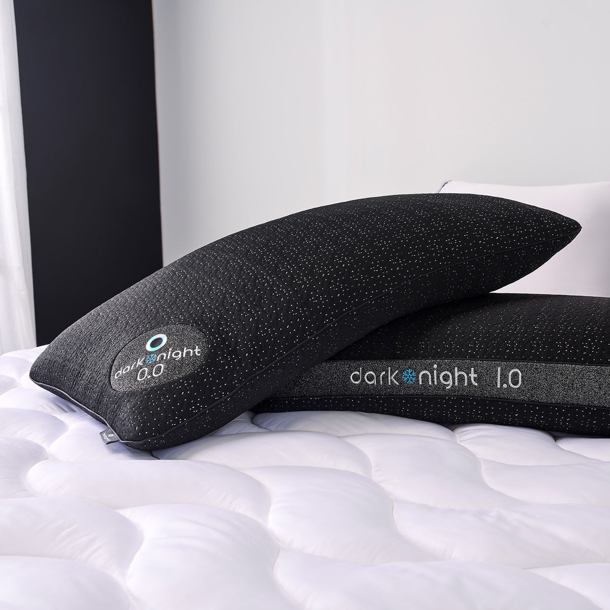 Two dark night pillows on a white quilted mattress in a bedroom setting.