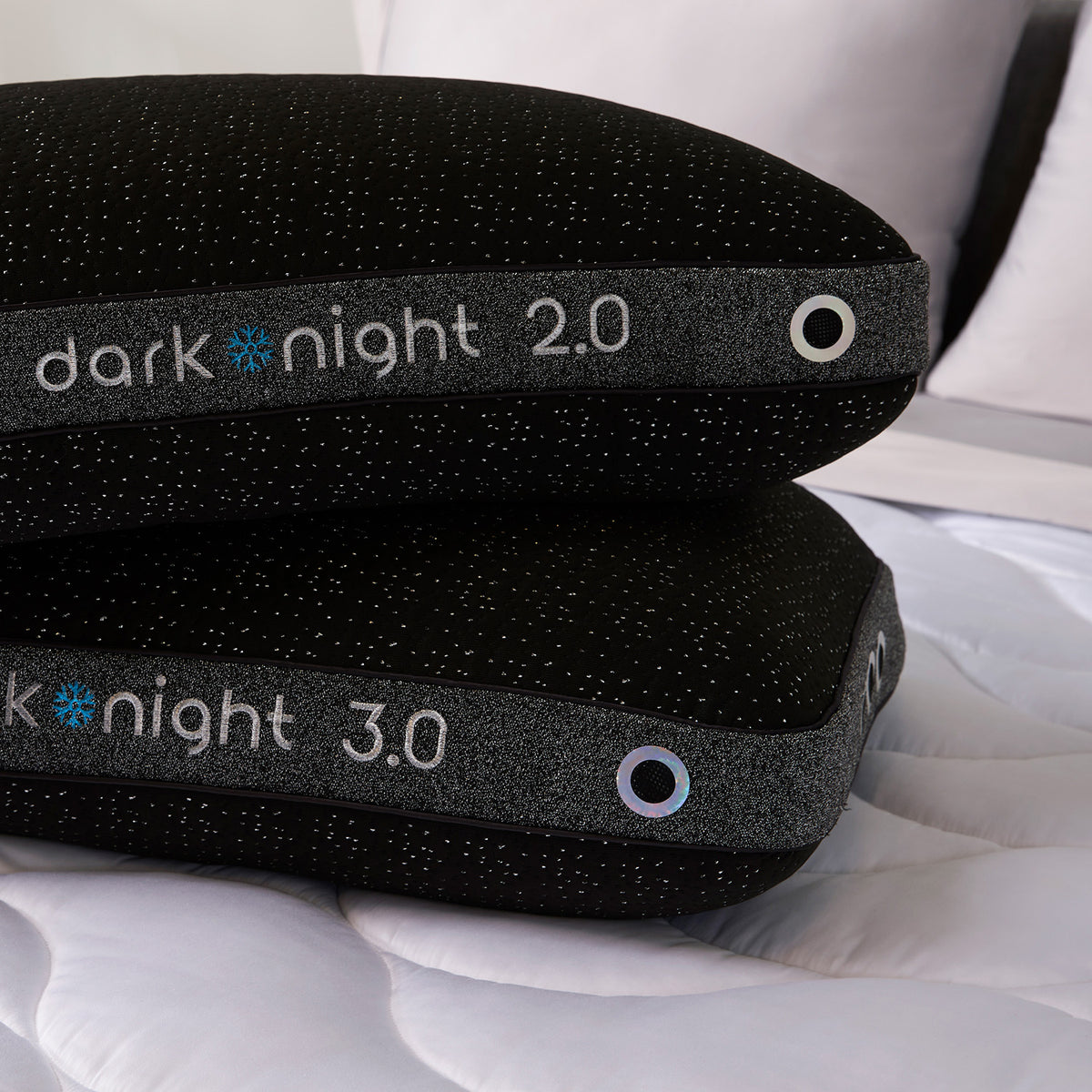 Two dark night pillows stacked on a white quilted mattress.