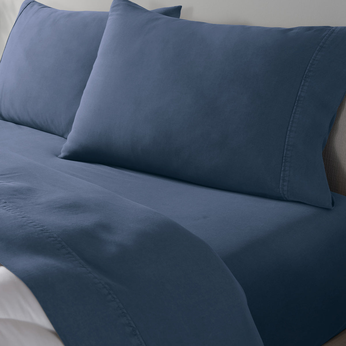 A close-up of a blue bedding set on a bed, showing a fitted sheet and two matching pillowcases.