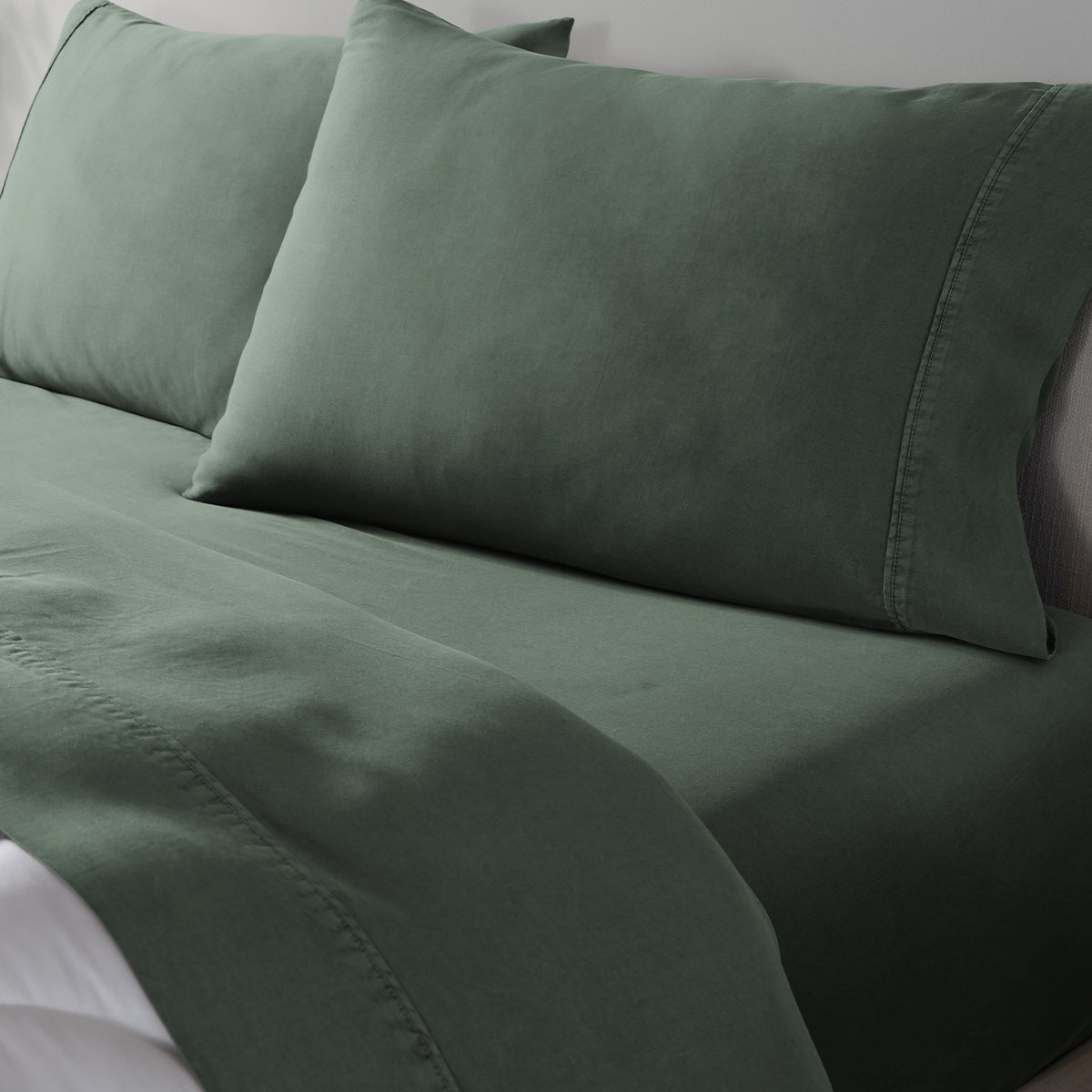 A close-up of a bed with matching dark green bedding, including a fitted sheet, pillowcases.