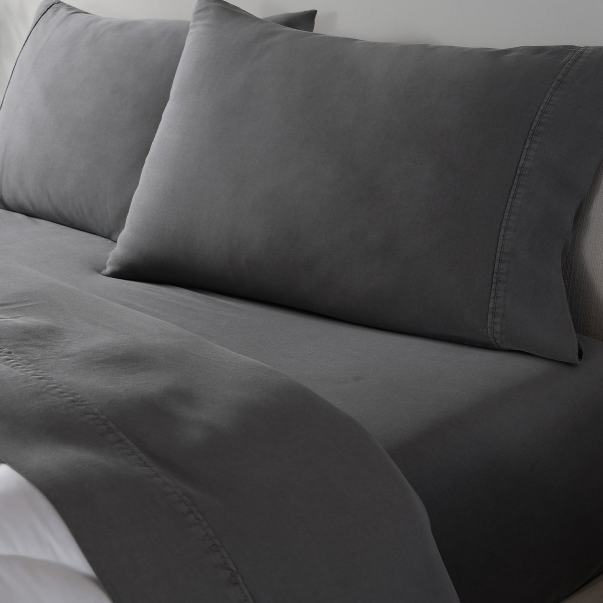 Dark gray bedding set including a fitted sheet and two matching pillowcases on a bed.
