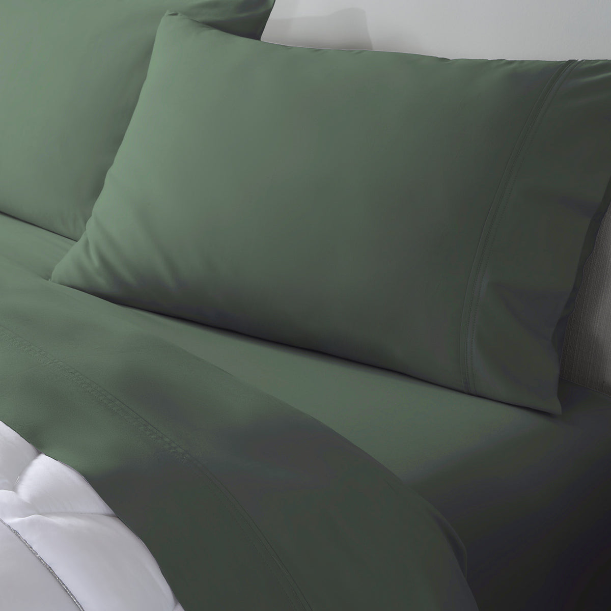 A close-up of a bed dressed in matching moss green bedding, including a pillowcases, and sheets.
