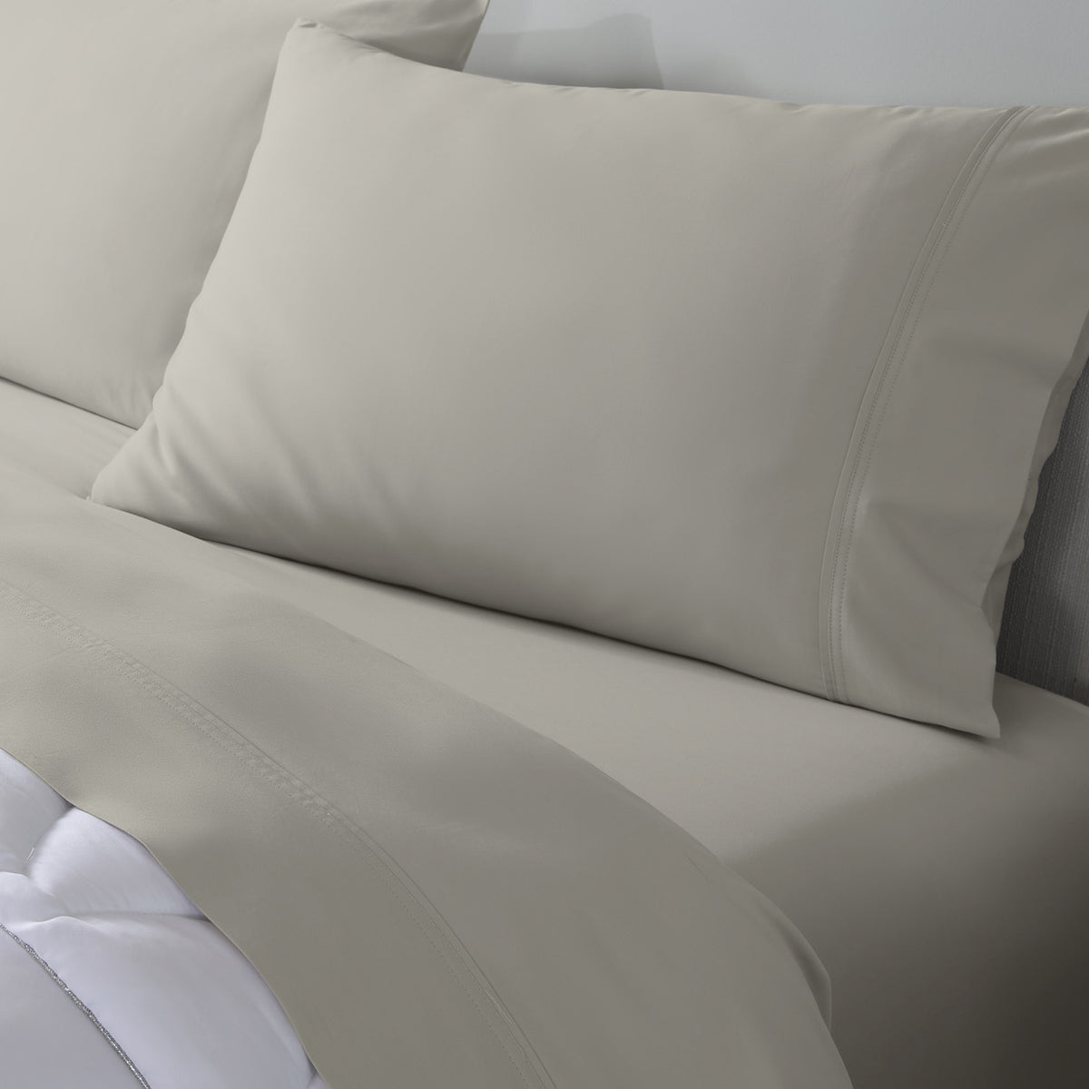 A close-up of a bed dressed in light taupe colored bedding, featuring  sheets, and pillowcases.