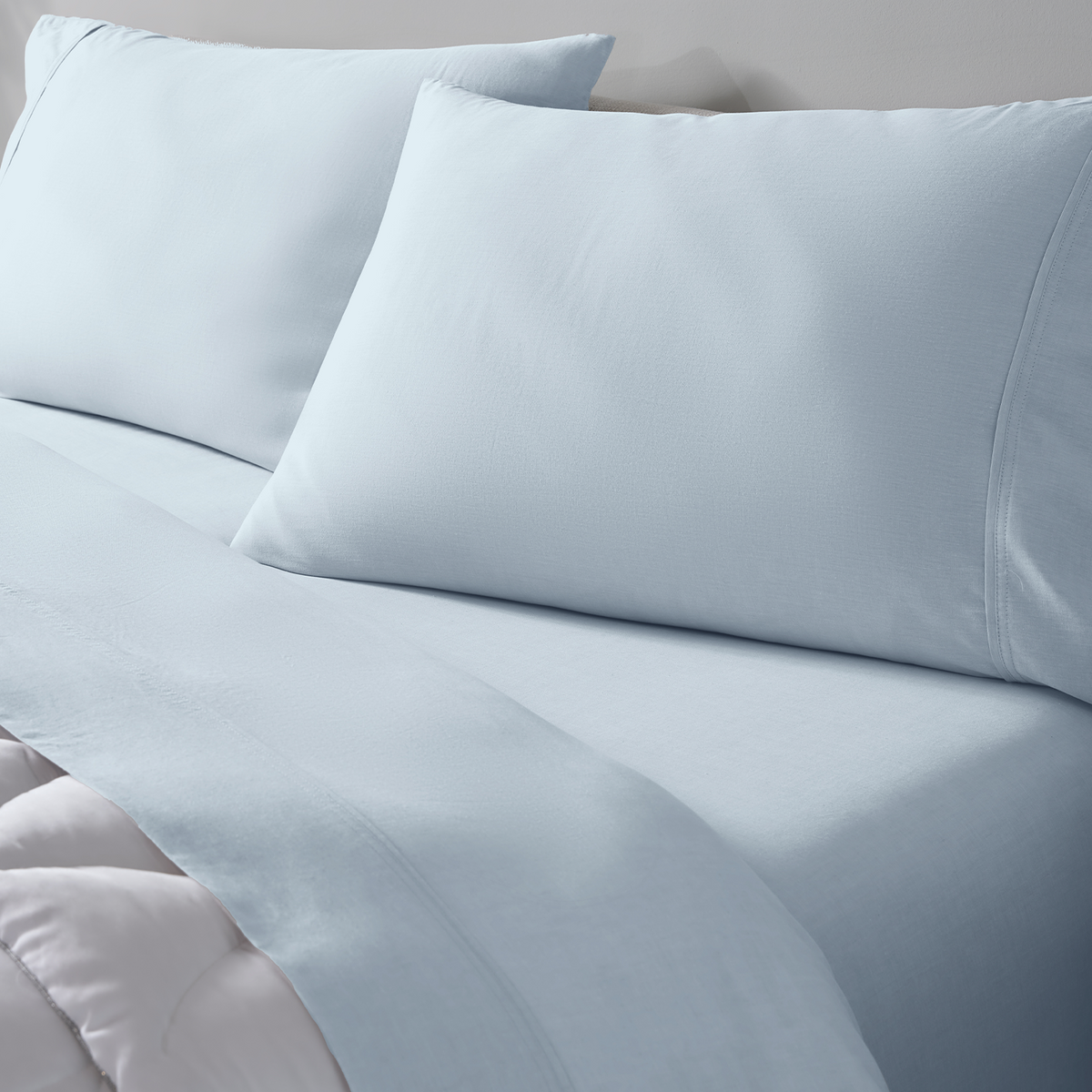 Light blue bedding set with two matching pillowcases and a fitted sheet on a bed.