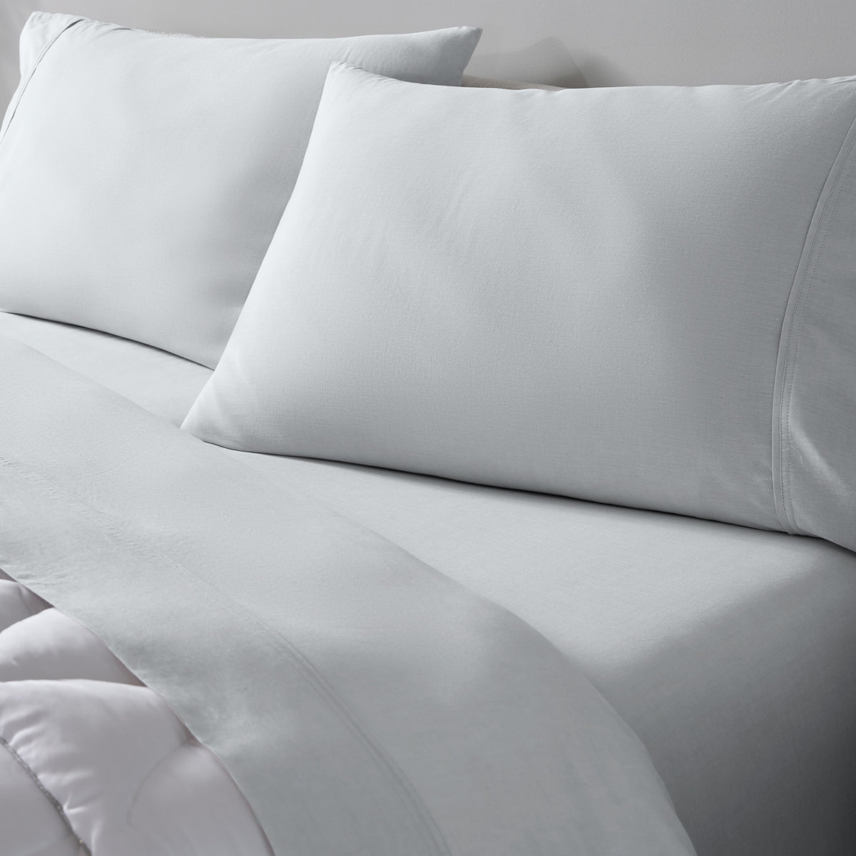 Light grey bedding set including two pillowcases and a matching sheet on a bed, photographed in a clean studio setting.