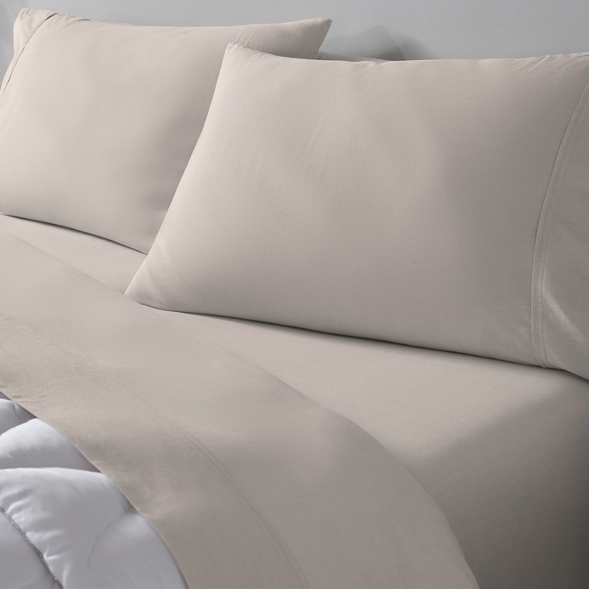 Taupe bed sheet set with two matching pillowcases on a bed, against a light gray wall.