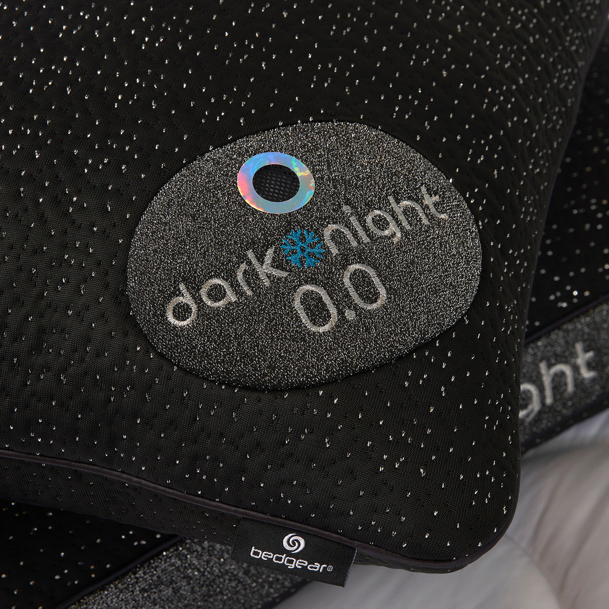 Close-up of a Dark Night pillow with a circular patch reading 'dark night 0.0' and a visible Bedgear brand tag near the bottom edge.