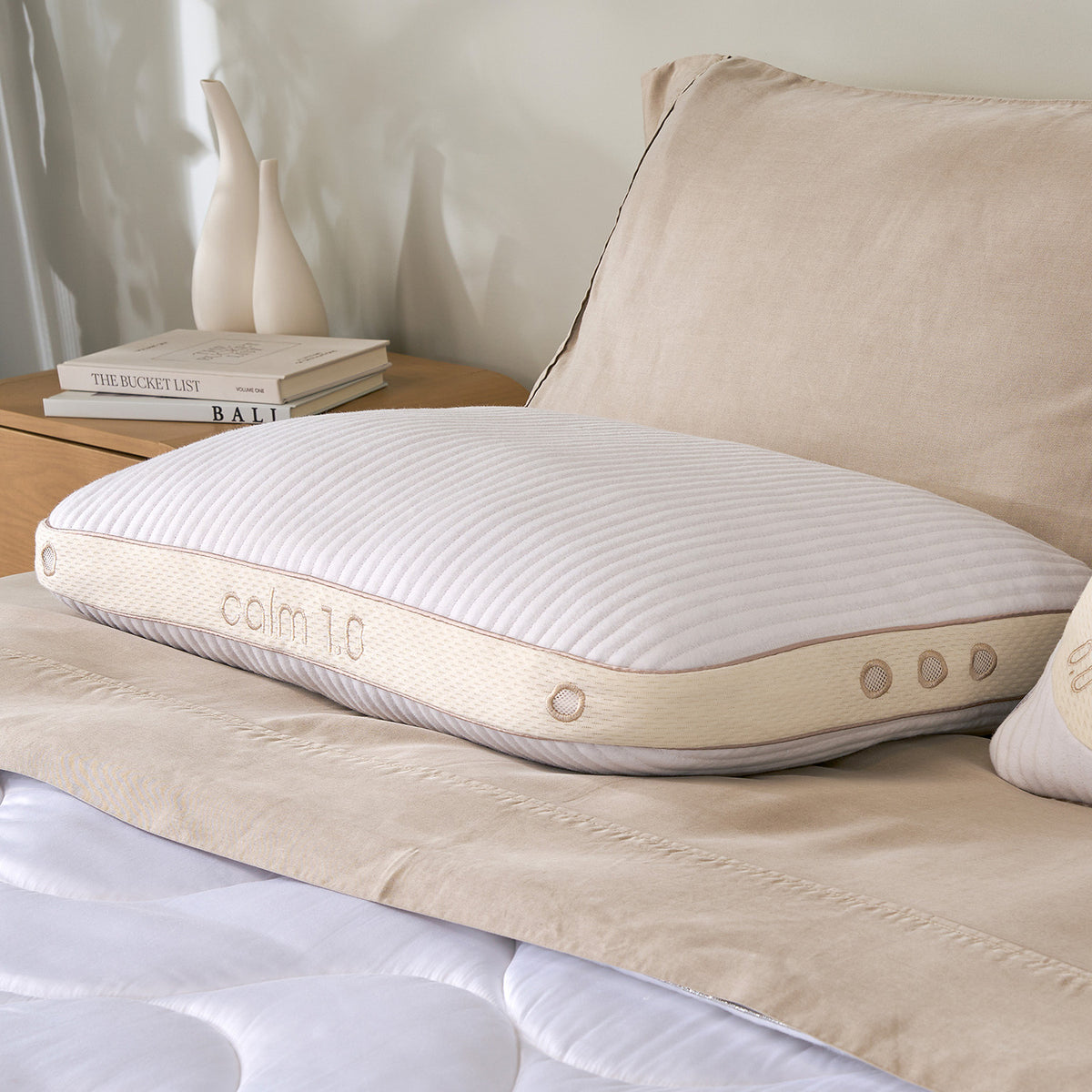 A close-up of a calm pillow resting on a beige quilted bedspread next to a matching pillow in a softly lit bedroom setting.