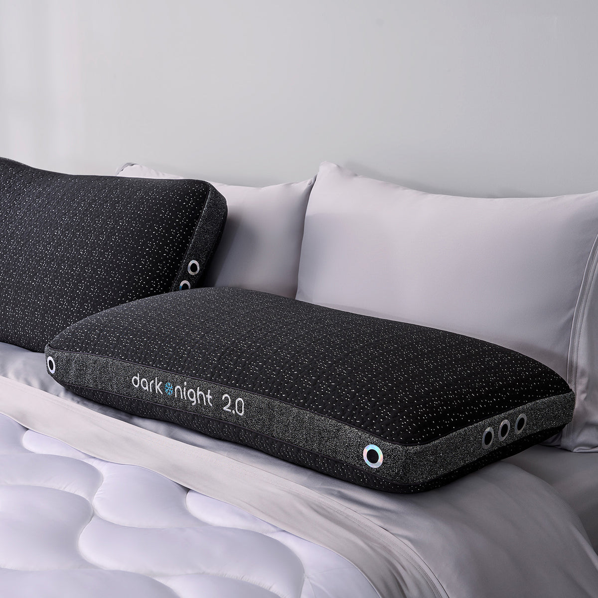 Two dark night 2.0 king pillows on a bed with white bedding.