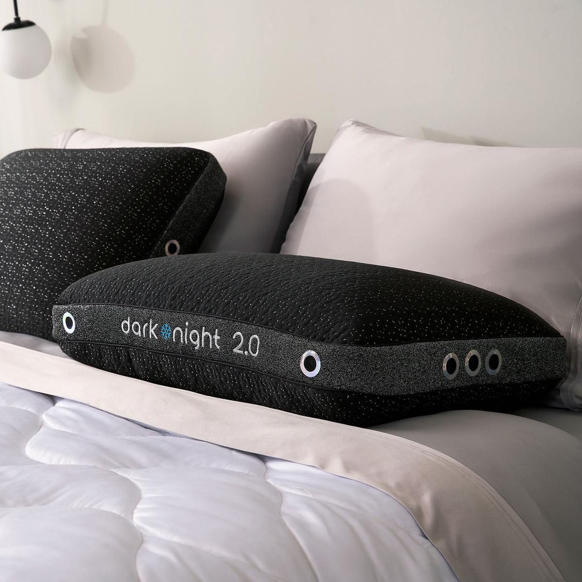 Two dark night pillows on a bed with white bedding and light gray pillows.