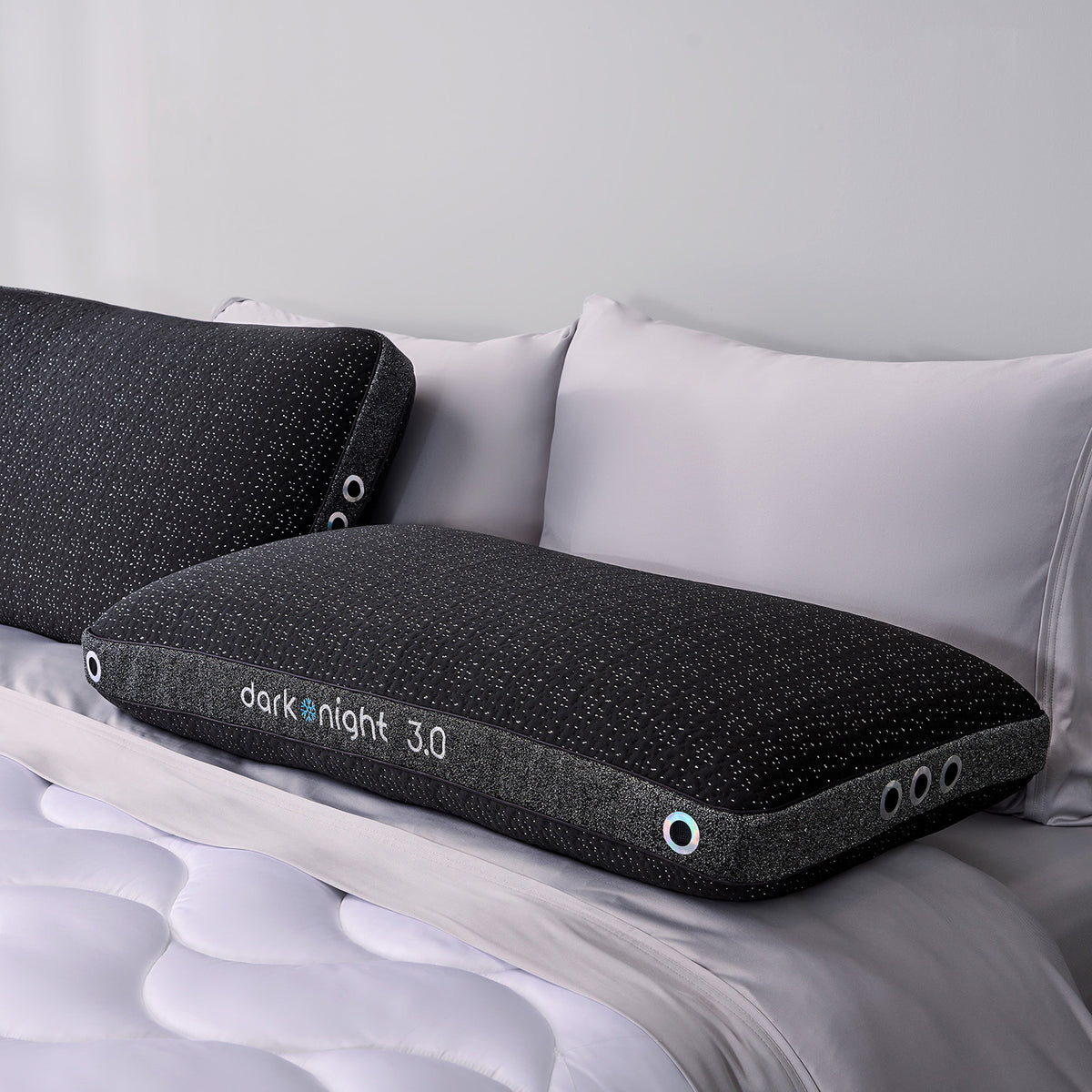 Two dark night 3.0 pillows on a bed with white bedding.
