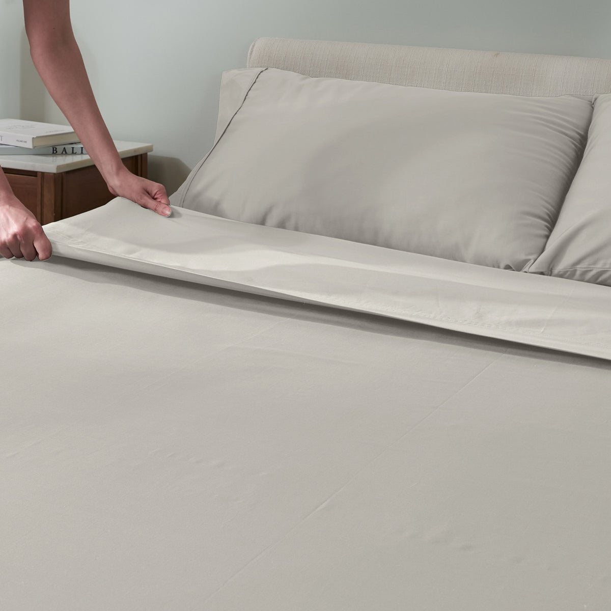 A person's hands are shown pulling a sheet across a bed.