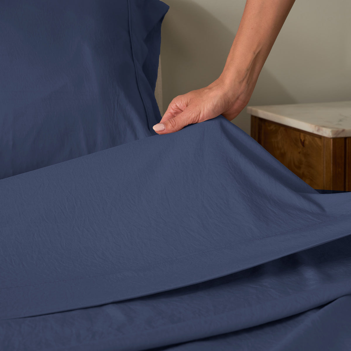 A woman making a bed with essential sheets.