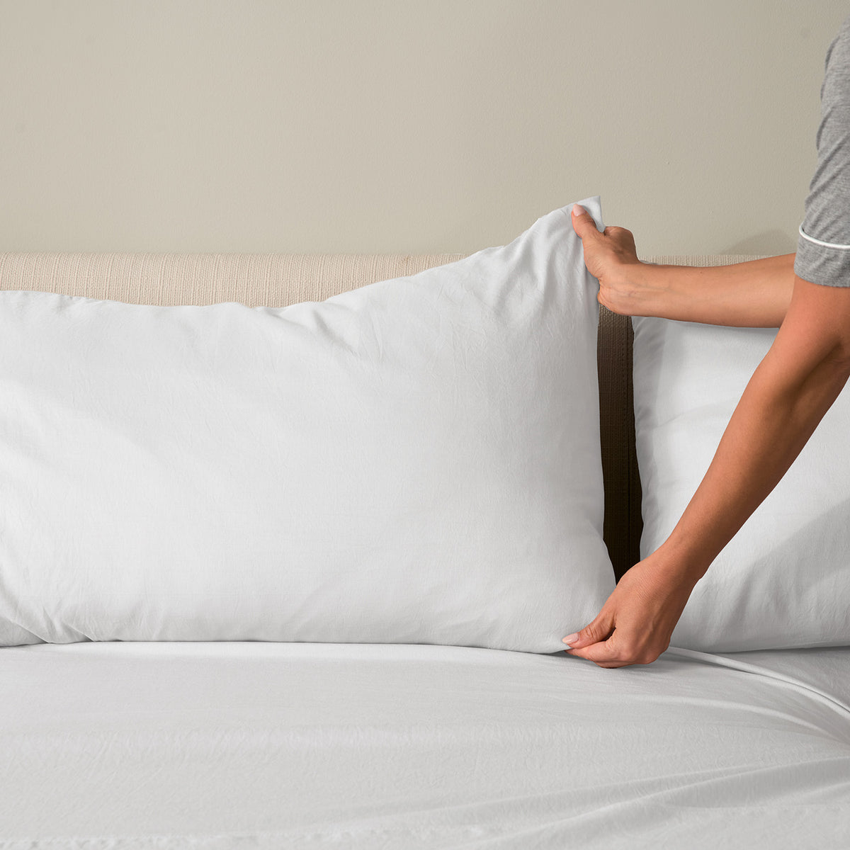 A woman making a bed with essential sheets.