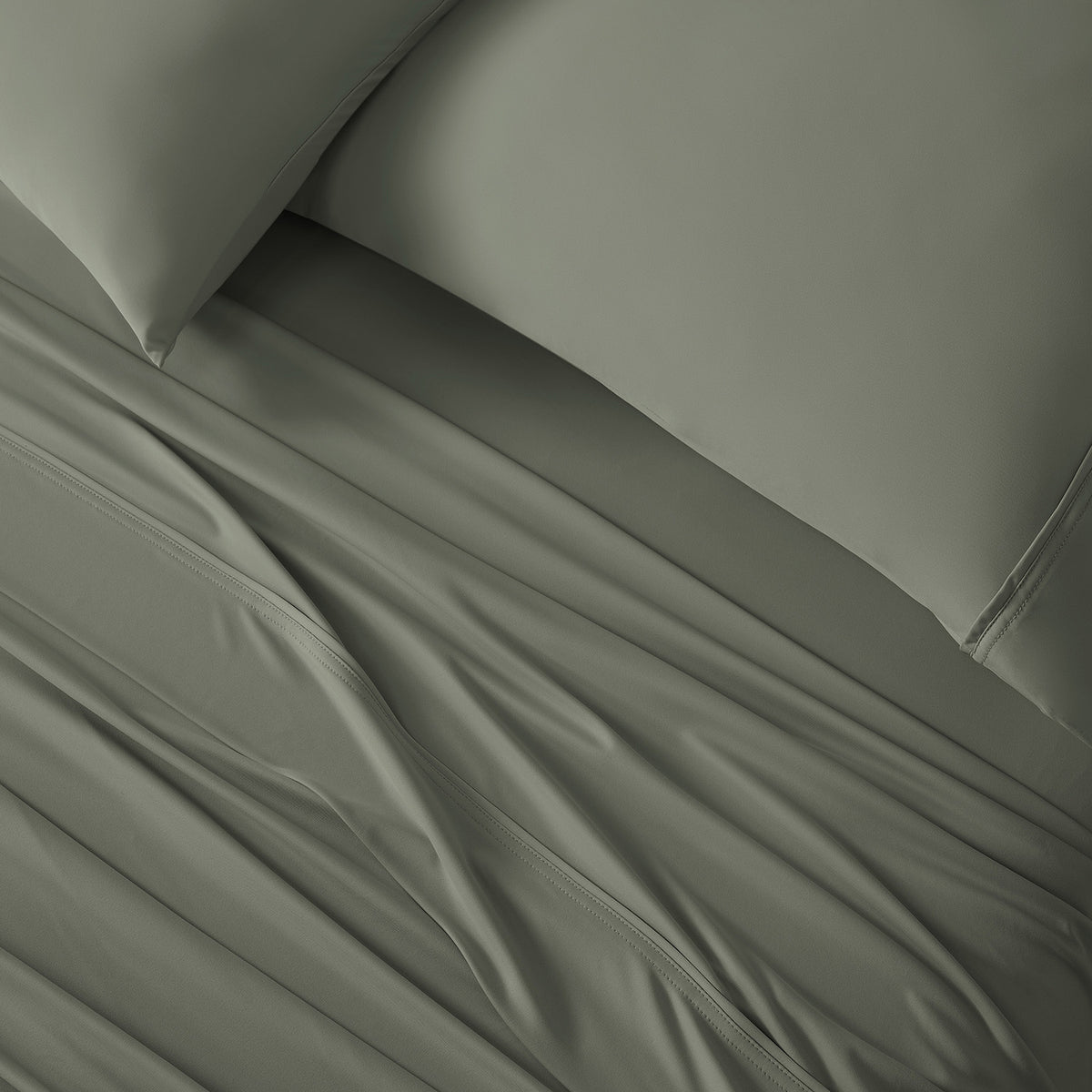 An image of two pillowcases and moss green VerTex sheets on a bed.