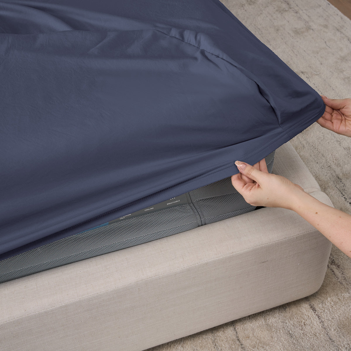 A woman pulling a fitted sheet over a mattress.