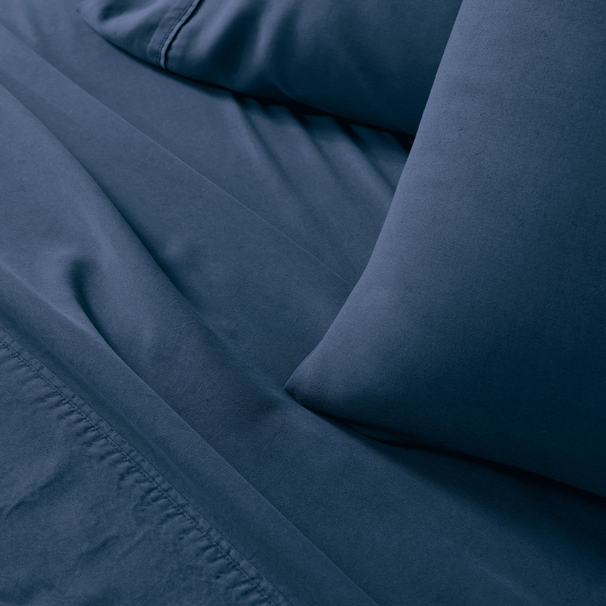 Close-up of indigo blue bedding fabric with a pillowcase and sheet, showing soft folds and stitched edges.