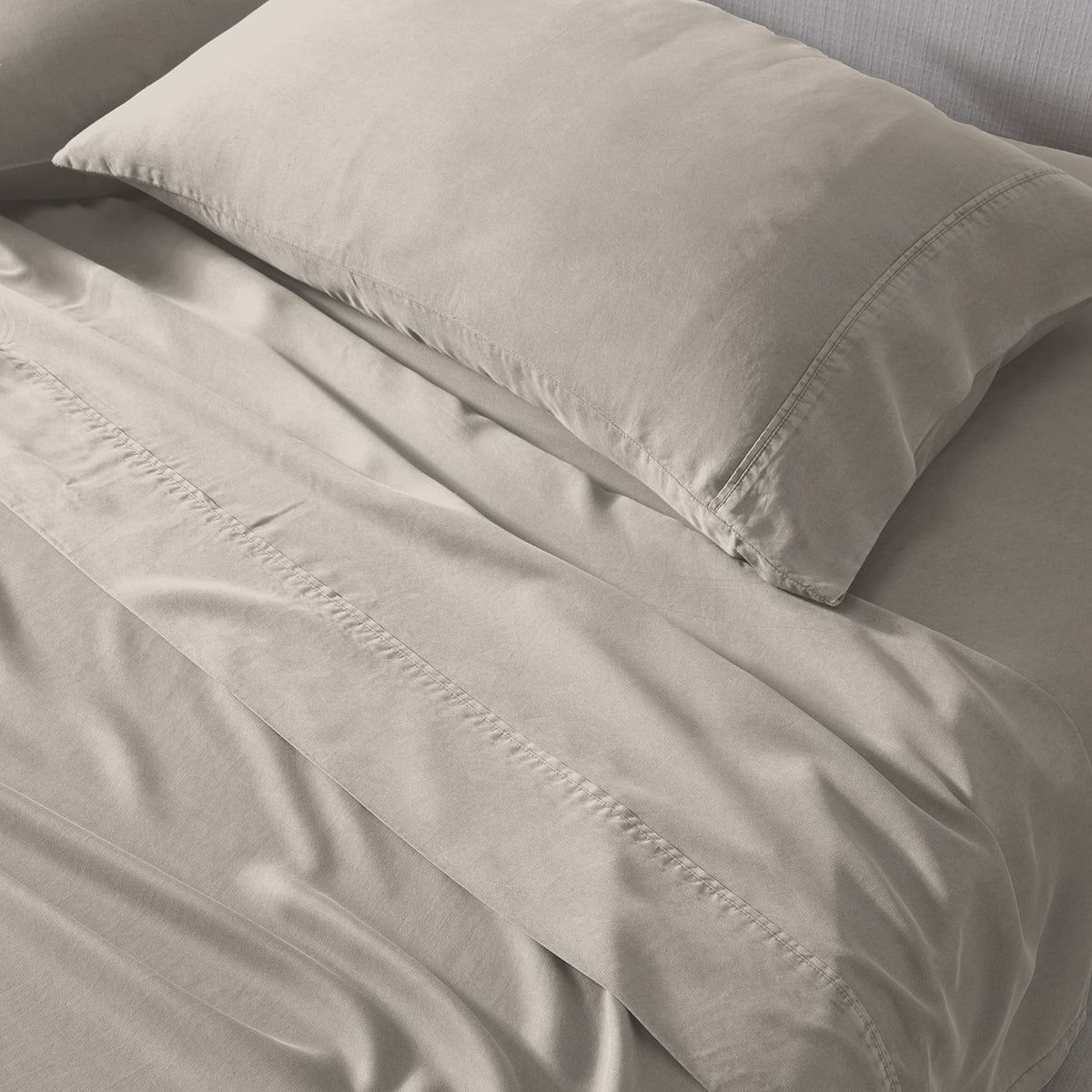 A close-up of a light beige bedding set, including a pillowcase and sheets.