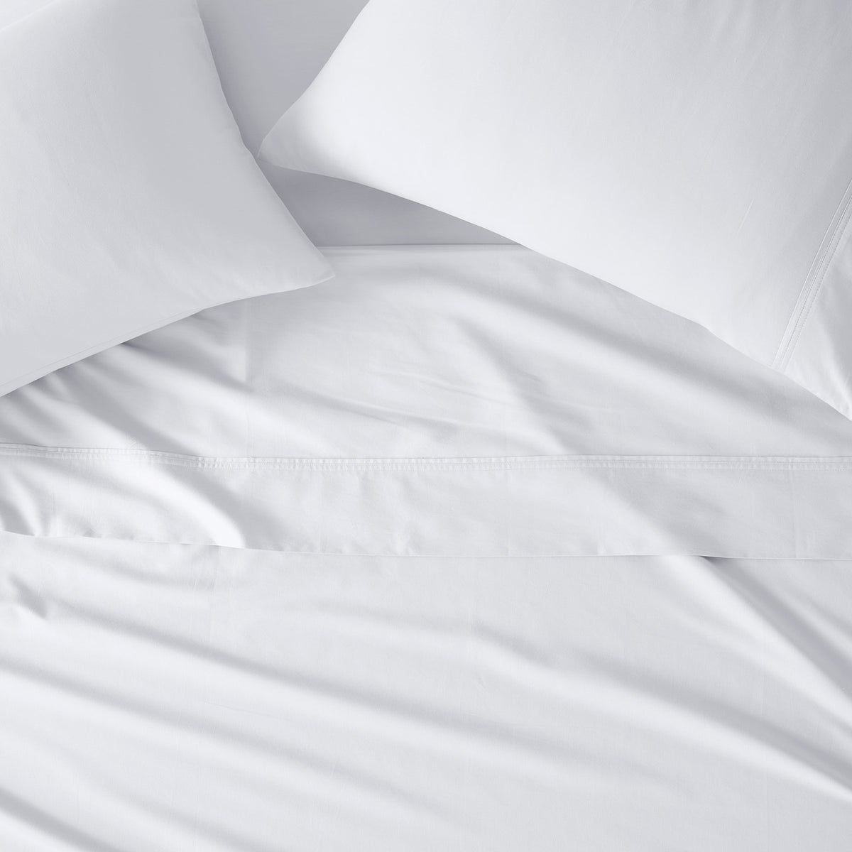 White bedding set with two pillows and a matching sheet, showing a close-up of the fabric texture and hem.