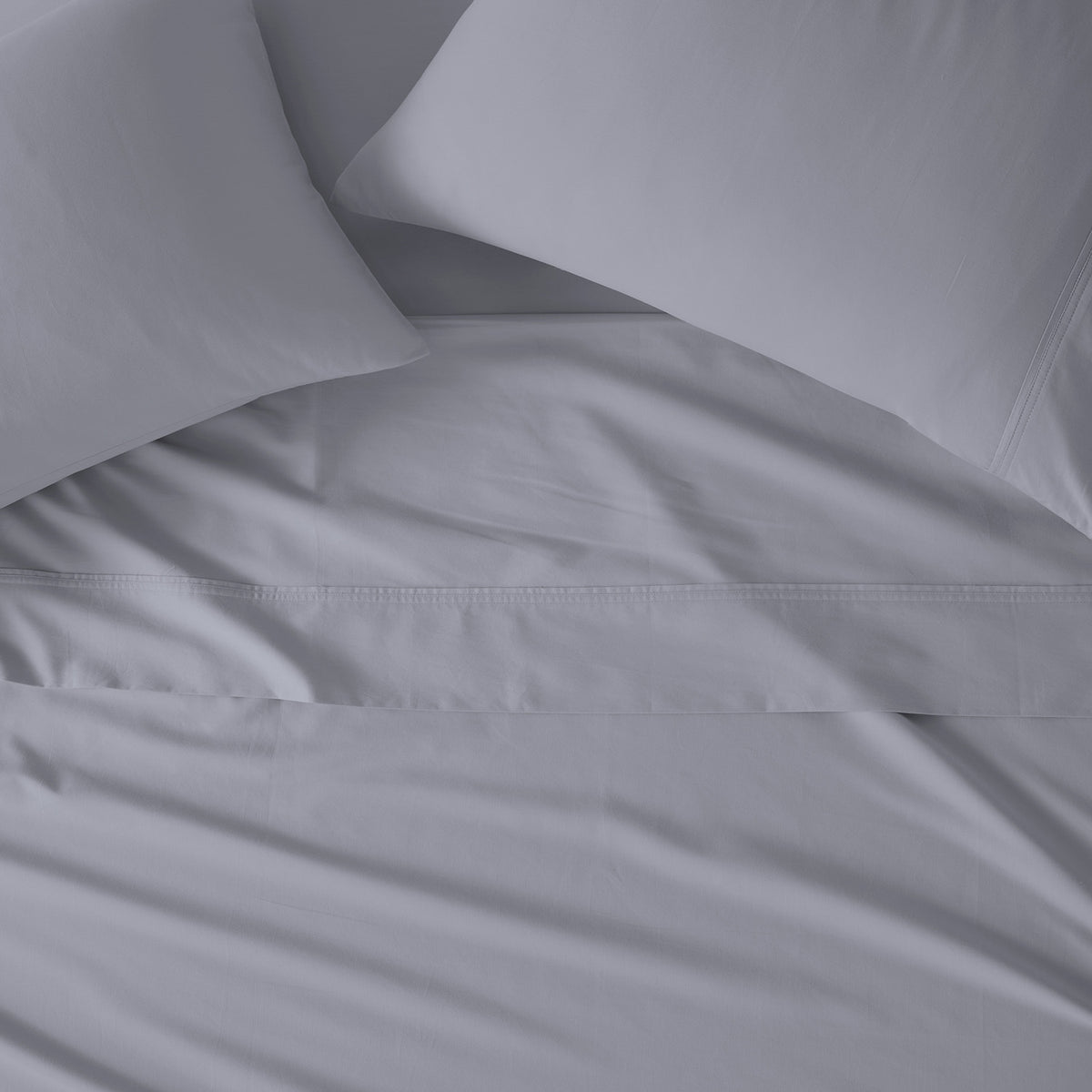 Light gray bedding set with two pillows and a matching sheet, showing a close-up of the fabric texture and hem.