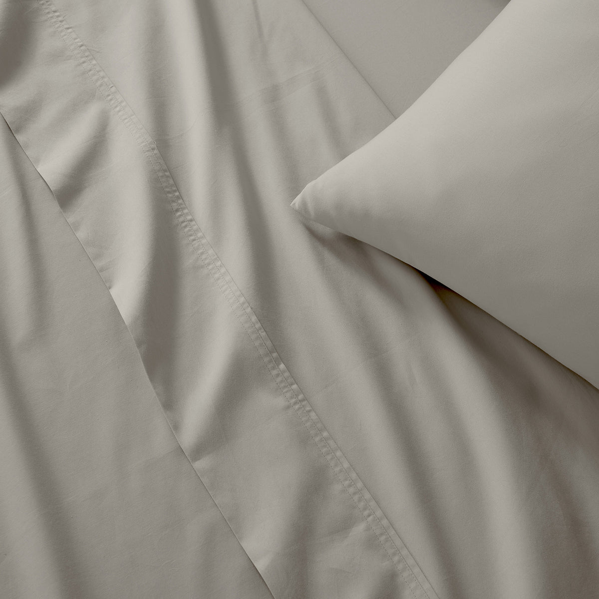Close-up of taupe bedding with a pillowcase, showing soft fabric folds and a stitched edge.