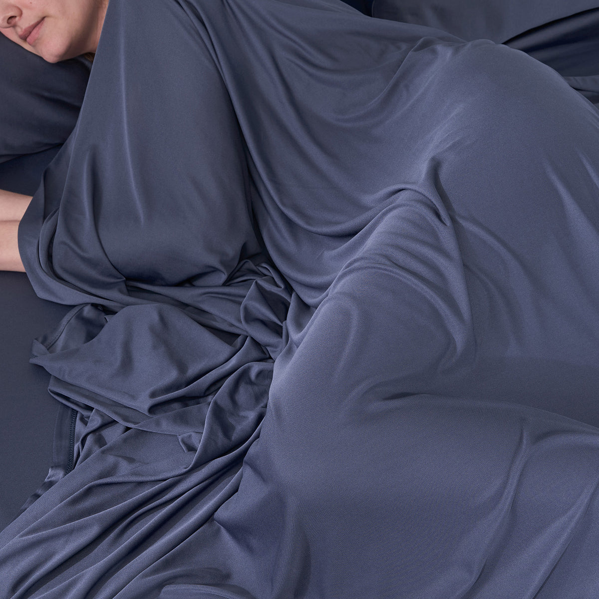 A woman lying in bed with blue DriTec sheets.