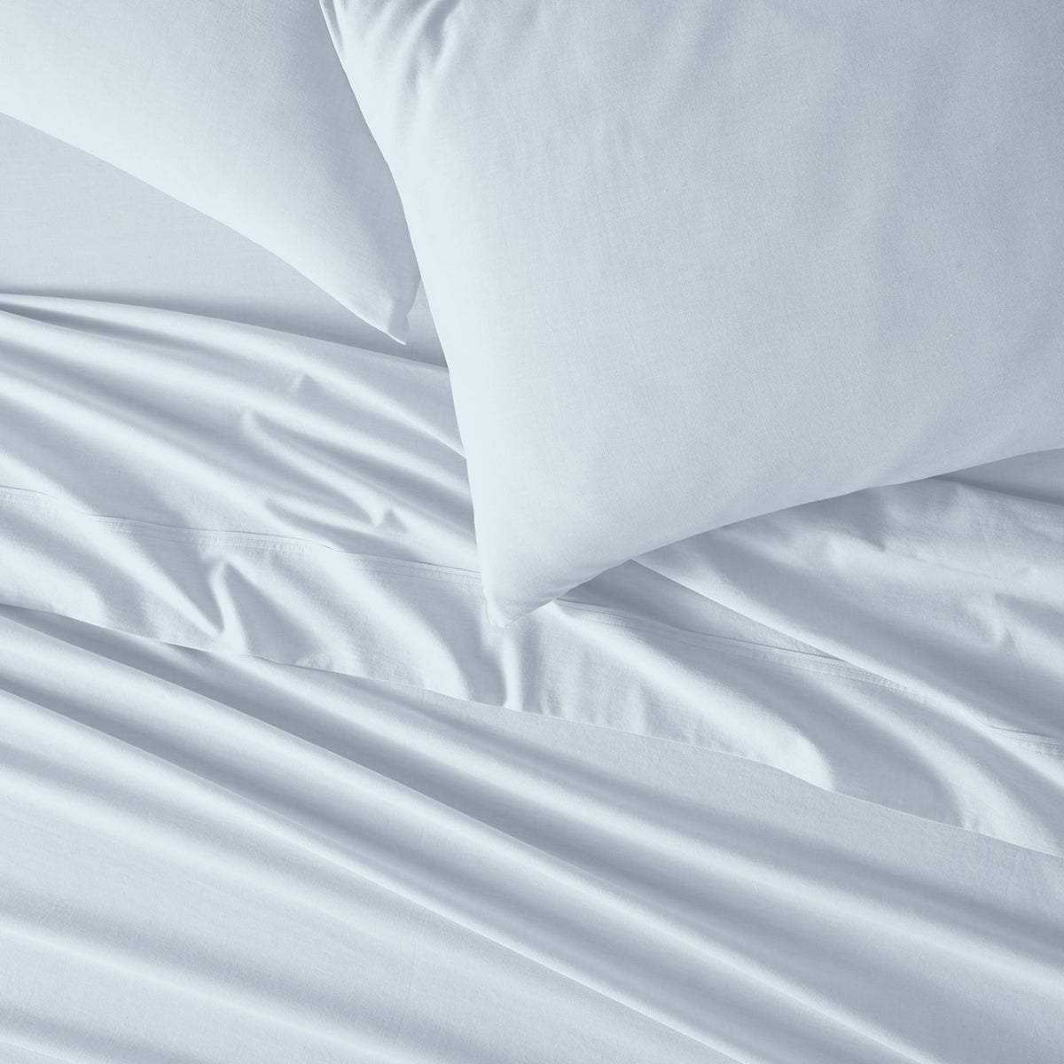 Light Blue bed sheets and two  pillows arranged on a bed, shown in a clean close-up shot.