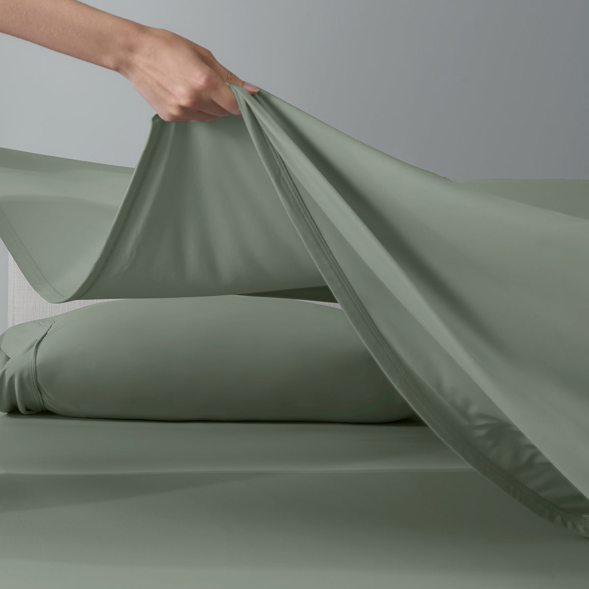 A woman putting moss green VerTex sheets on a mattress.