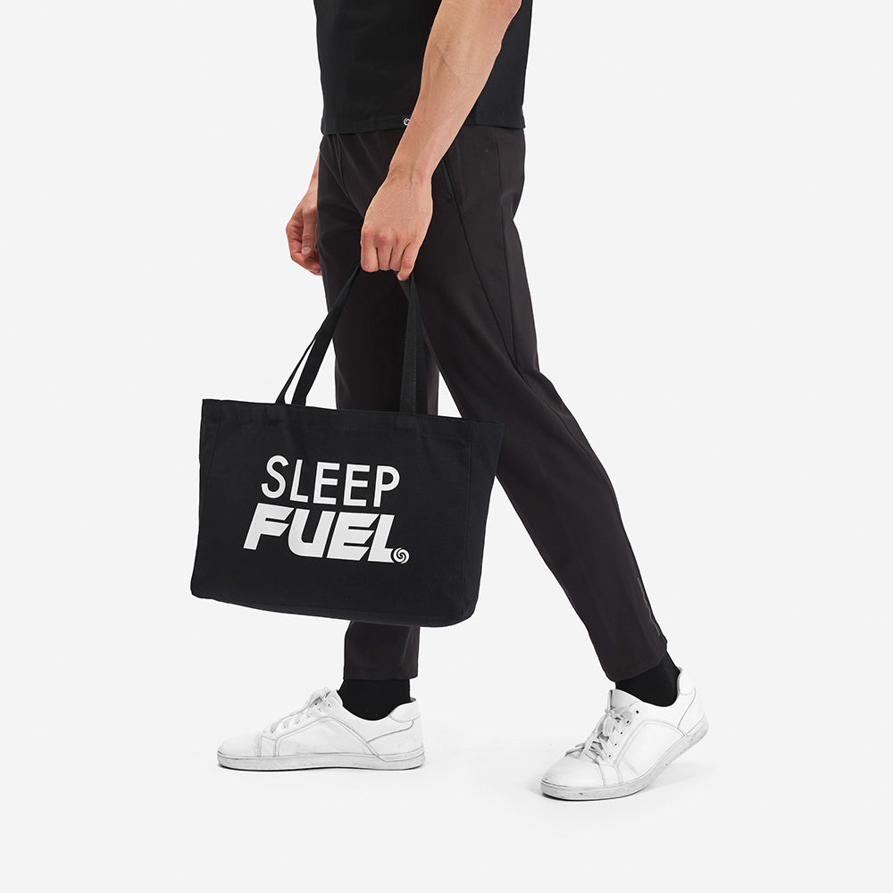 A man holding a Sleep Fuel tote bag in front of a white background. 