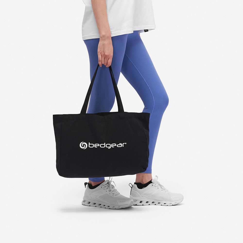 A woman earing blue leggings carrying a BEDGEAR tote bag. 
