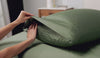 A woman folding a pillowcase over a pillow. 