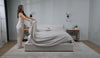 A woman making a bed with linen bed sheets. 